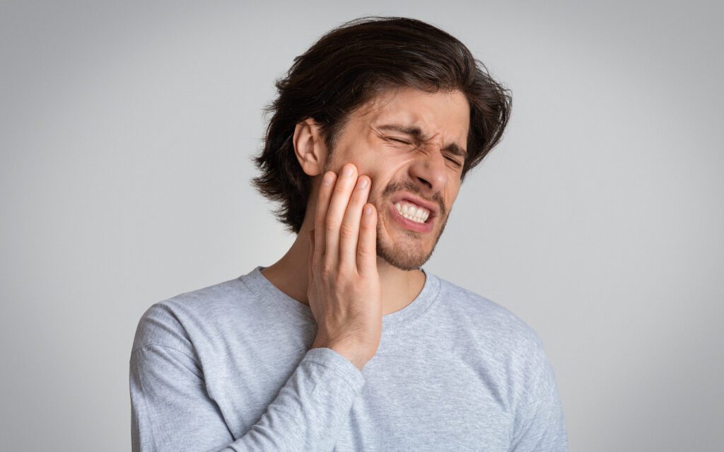 A man with his mouth open, displaying his teeth while holding them in his hands, showcasing a pained expression.